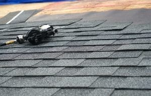 A nail gun resting on an asphalt shingle roof in the process of being installed